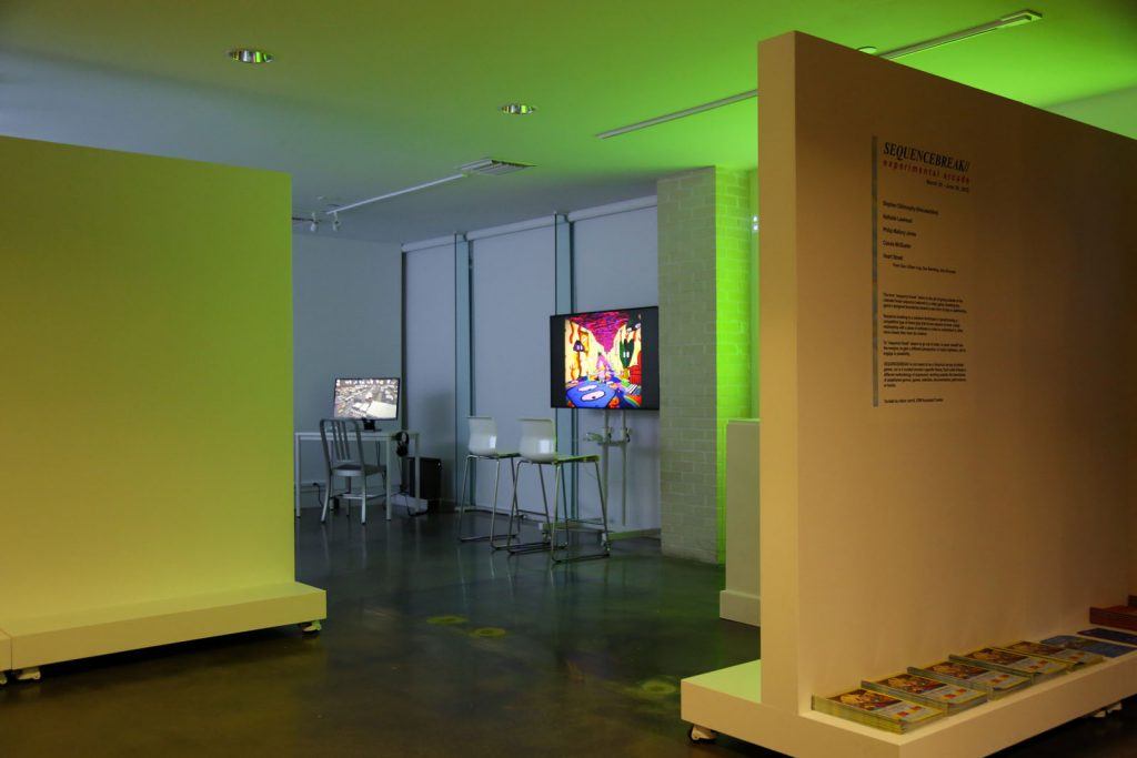 Darkened art gallery with two video screens visible in the background.