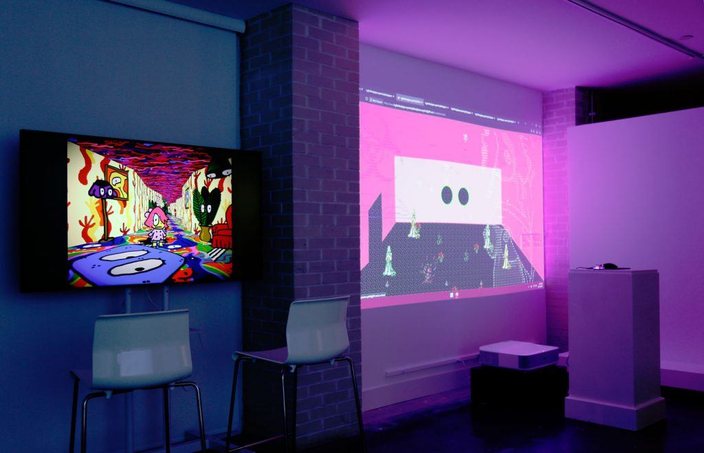 A large monitor and projection in a darkened art gallery.