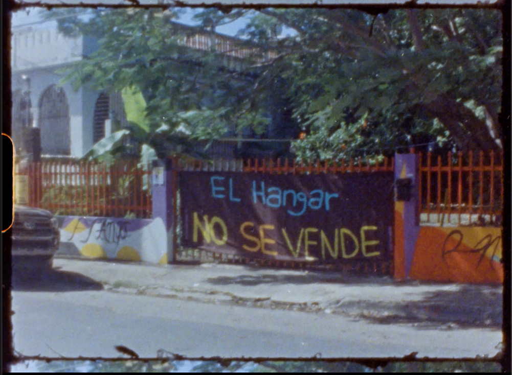 16mm film still of a sign that reads "El Hangar No Se Vende."