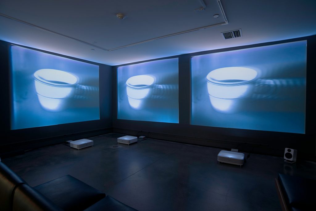 Three projected images of a coffee cup in a gallery space.