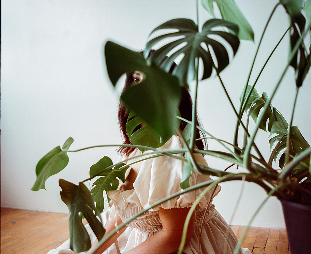Photograph of a person sitting behind a plant with their eye showing through.