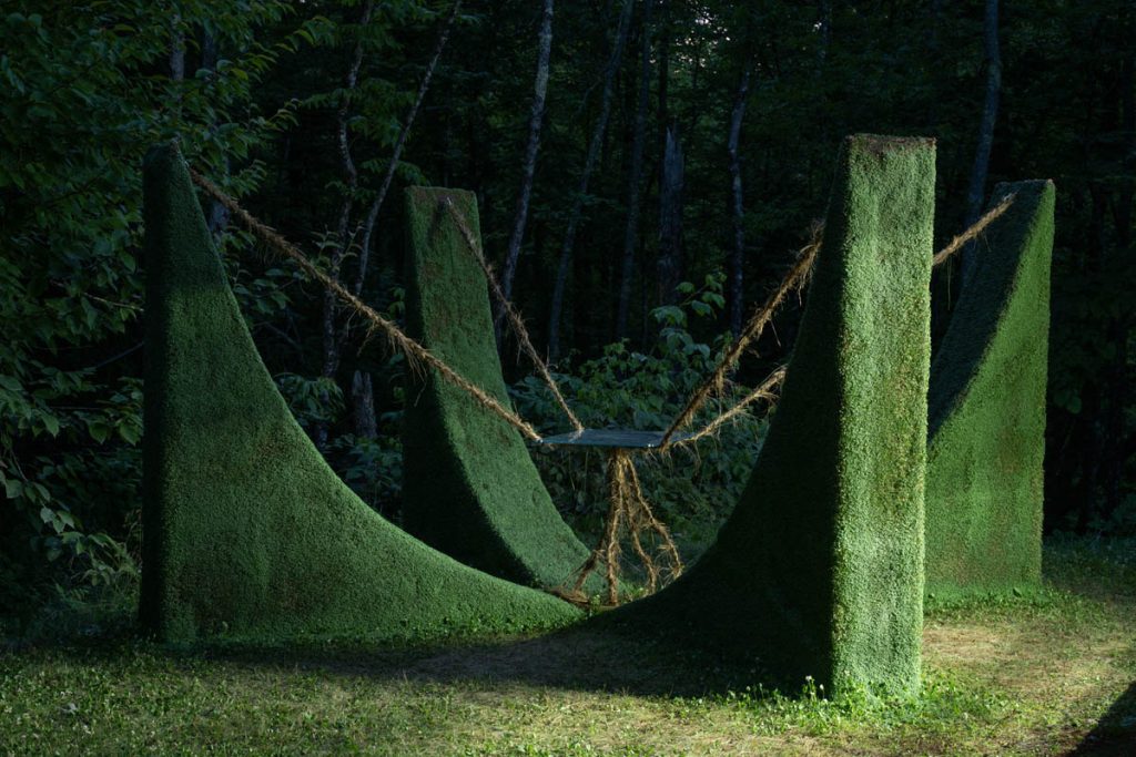 Photograph of a green environment with an object suspended in the middle of four pillars.