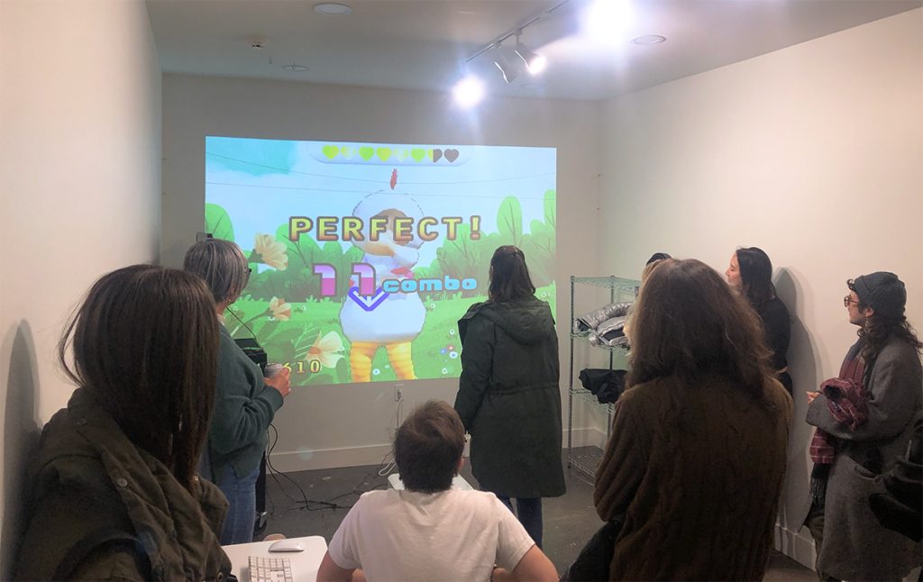 A group of people in a studio space looking at a projected video game image.